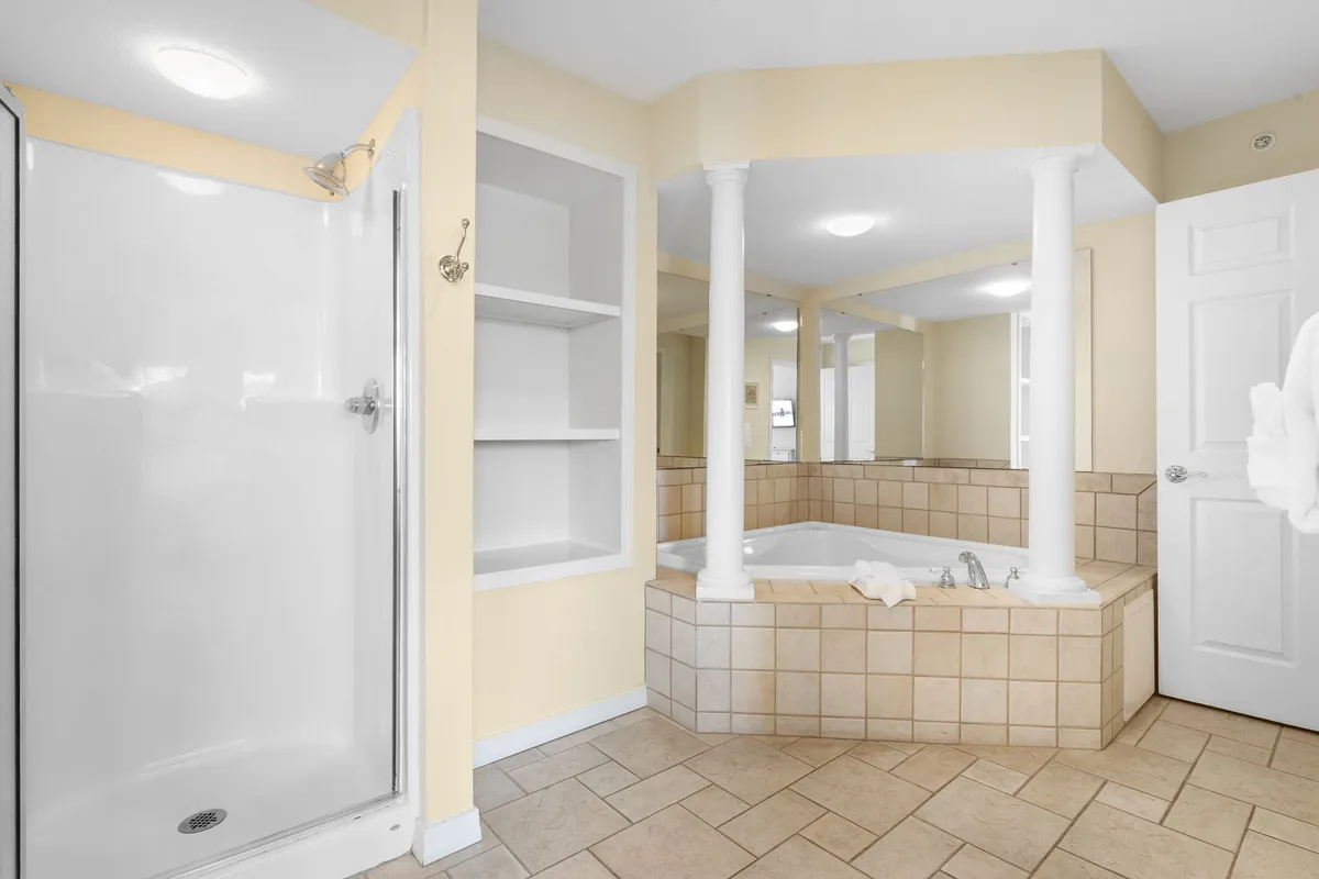 A serene bathroom scene with a soaker bathtub, elegant pillars, a mirrored wall, and a shower area. The design exudes a spa-like ambiance, inviting guests to unwind and indulge in luxurious self-care.