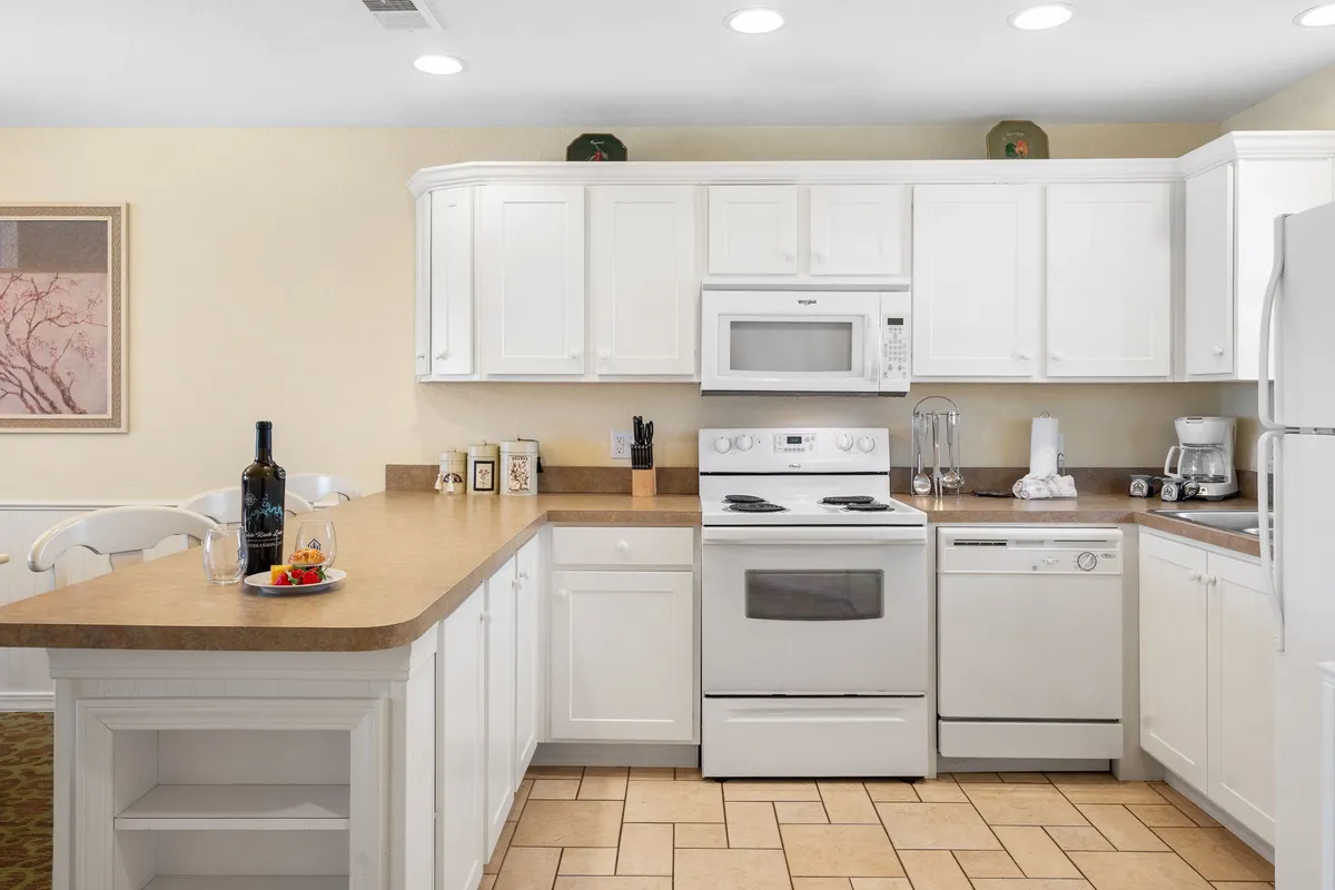 A bright kitchen with crisp white cabinetry, a well-appointed countertop set with wine and fruit, and modern appliances like a stove and dishwasher. The setup encourages both everyday cooking and special occasions.