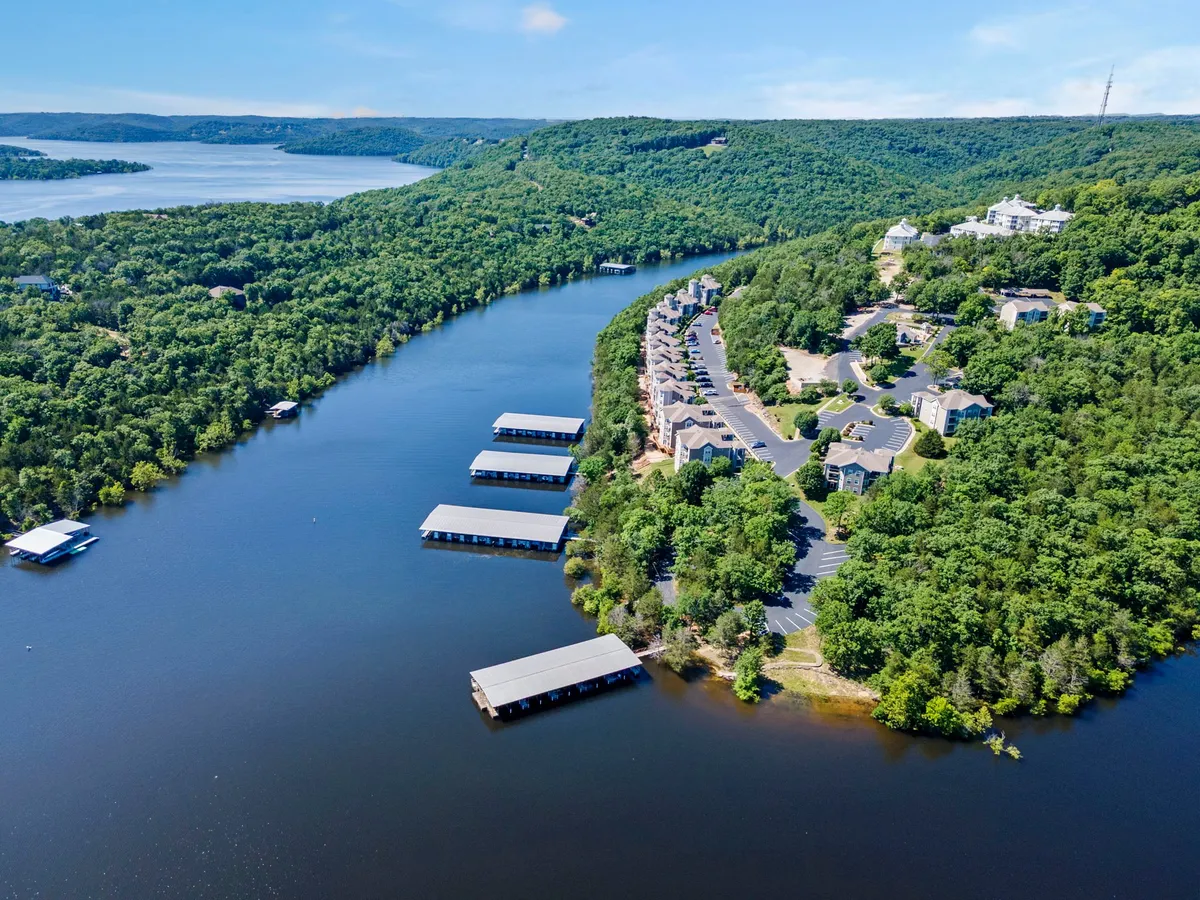 A serene panoramic lake view, with marinas, lush greenery, and residential buildings dotting the landscape. The calm waters and inviting surroundings evoke the excitement and relaxation of boating, fishing, and swimming as a family.