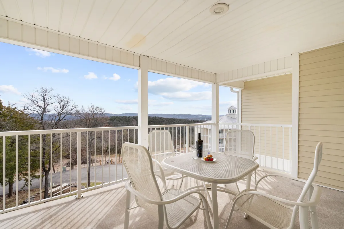 An outdoor patio table set with a bottle of wine and strawberries, surrounded by comfortable seating. The scene overlooks a sweeping landscape, hinting at sunset or early evening, with a calm, relaxed ambiance perfect for couples or friends. The setup suggests an intimate setting to enjoy scenic Ozark views and tranquil moments together.