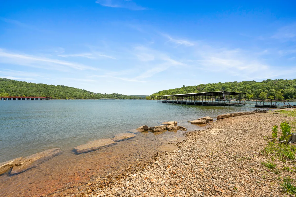A panoramic view of a calm lake with distant green hills, a small boathouse, and a rocky shoreline. The scene evokes tranquility and outdoor adventure, ideal for water sports or a lakeside picnic.
