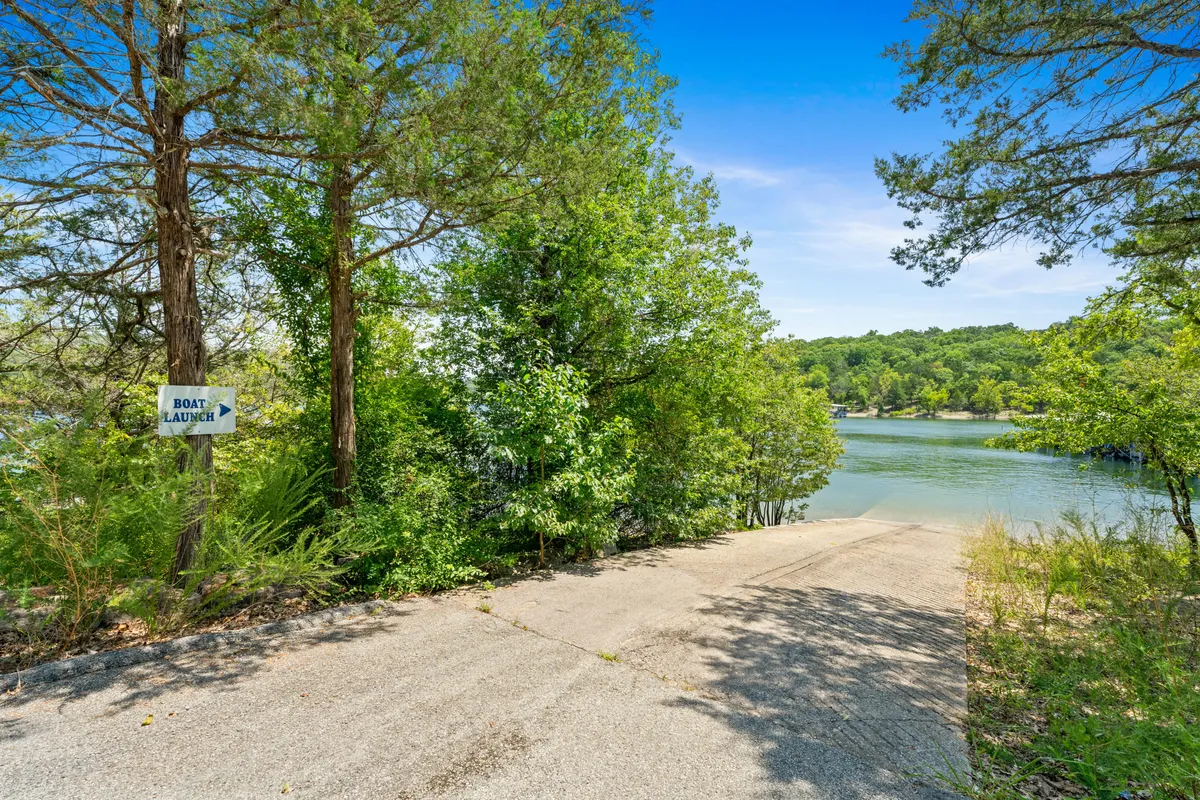 A concrete boat ramp leading directly into Table Rock Lake, bordered by green trees. A sign marks the boat launch, and the calm water invites boating or fishing adventures, with a gentle, relaxed lakeside mood.