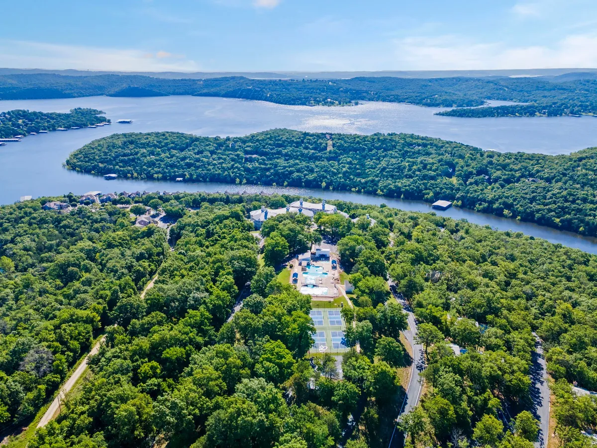 This image features an expansive view of Table Rock Lake with surrounding greenery and visible property amenities, including a pool and tennis courts. The scene is tranquil and inviting, capturing the outdoor recreation facilities available to guests as well as the beautiful lakeside setting.