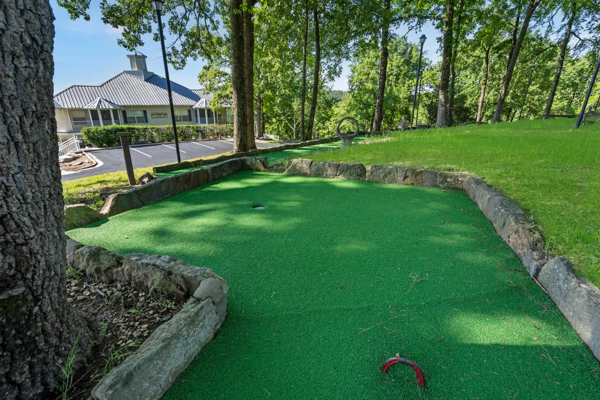 A vibrant mini-golf area set among lush greenery with stone edging and playground equipment visible in the background. Families and children are seen enjoying mini-golf and outdoor games, hinting at a relaxed, playful atmosphere.