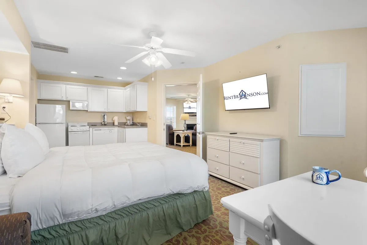 The photo showcases a cozy bedroom with a bed, an adjacent kitchenette area, television, and a dining table. The room is designed for comfort and convenience, offering guests the ability to enjoy in-room meals or coffee with ease.