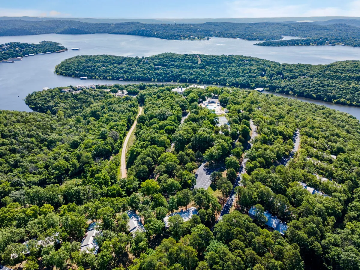 A serene view of lush green trees, calm sparkling water, and homes nestled in nature. The image radiates peace and invites exploration, with the landscape ideal for hiking, boating, and relaxing by the water.